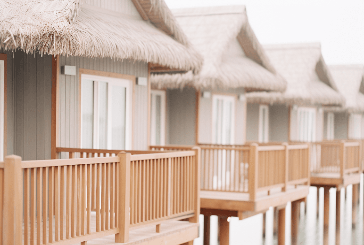 Overwater villas with thatched roofs standing on stilts above a calm tropical lagoon