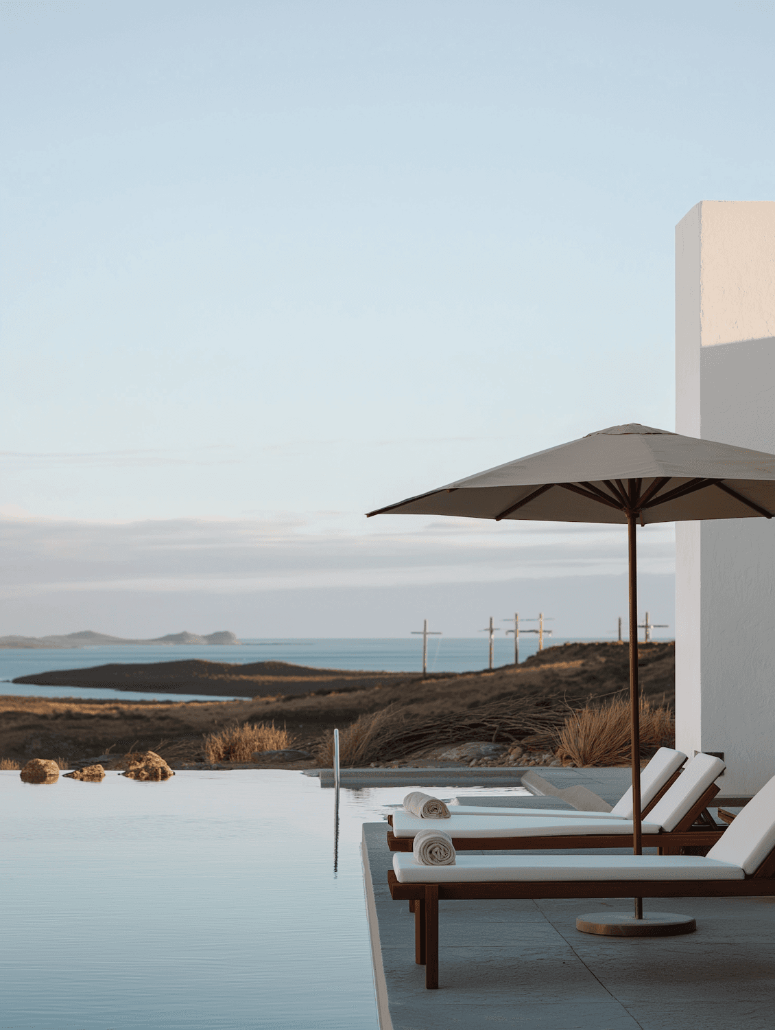 An infinity pool with wooden loungers overlooking the coast under a soft blue sky